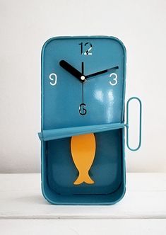 a blue clock with a yellow fish on it's face sitting on a white surface