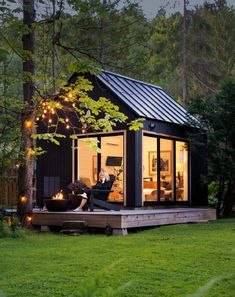 a woman sitting on a deck in front of a small cabin with lights strung from the roof