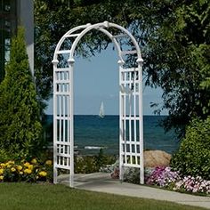 an arch in the grass near flowers and water