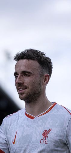 a man with curly hair standing in front of a soccer field wearing a red and white uniform