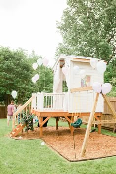 a wooden play set in the middle of a yard with white balloons floating around it