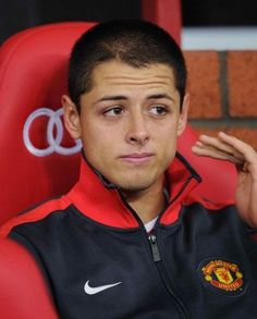 a young man sitting in a red chair with his hand on his chin and looking at the camera