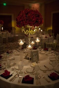 the table is set with white linens and red rose centerpieces, candles and place settings