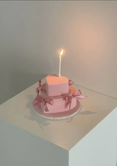 a pink heart shaped cake with a candle on it sitting on a white table top