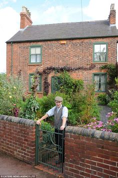 a man leaning on a fence next to a brick house