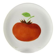 a white plate with an orange painted on the side and green leaves sticking out of it