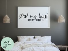 a bed with white sheets and pillows in front of a wall hanging above it that says steal my heart not my blankets