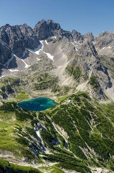 the mountains are covered in green grass and blue water, with a small lake surrounded by snow - capped peaks