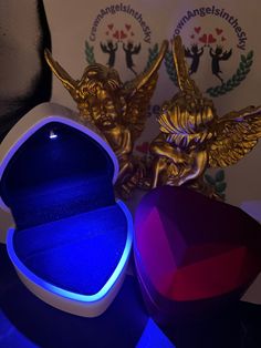 an open ring box sitting on top of a table next to two angel figurines