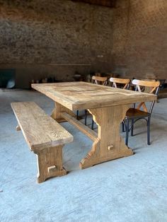 a wooden table and benches in a room with brick walls, concrete flooring and exposed ceilings