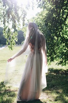 a woman in a wedding dress standing under a tree with her veil blowing over her head