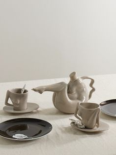 a table topped with plates and cups filled with saucer, spoons and coffee pot