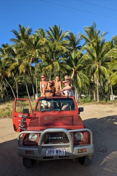 four people are sitting in the back of an old pickup truck with palm trees behind them