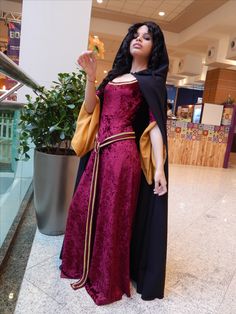 a woman dressed up in a costume holding a flower and standing next to a potted plant