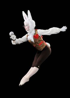 a woman dressed in bunny ears and holding an alarm clock while jumping into the air