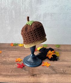 a crocheted hat sitting on top of a wooden table next to autumn leaves