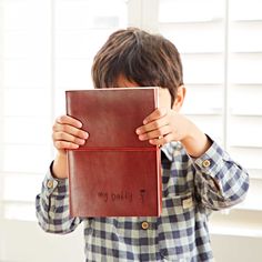 a young boy holding up a book with the words my daddy written on it in front of his face