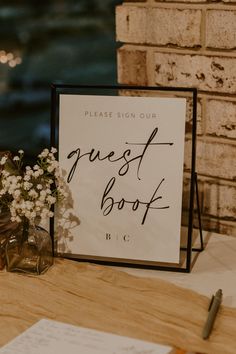 a sign that says guest book next to some flowers on a table with paper and pen