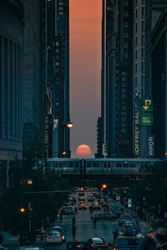 the sun is setting behind tall buildings in an urban area with cars driving down the street