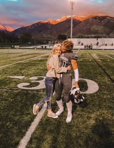 two people standing on a football field with mountains in the background