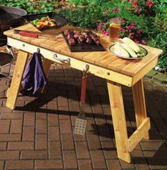 a wooden table sitting on top of a brick patio next to a grill and potted plant