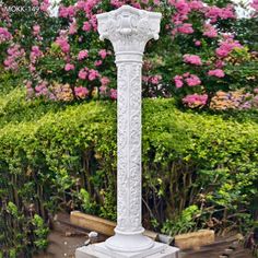 a tall white pillar sitting in the middle of a flower filled garden with pink flowers behind it