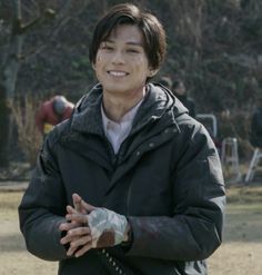 a young man is smiling and holding his hands out to the side while standing in a park