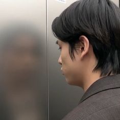 a man with black hair standing in front of a metal door