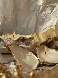 three candles sitting on top of oysters in front of some gold foiled paper