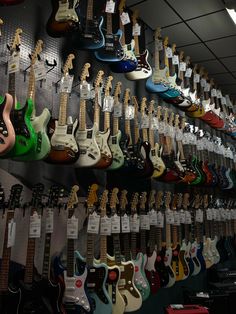 guitars are lined up on the wall for sale