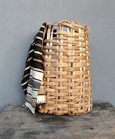 a woven basket sitting on top of a wooden table next to a wall with a blanket