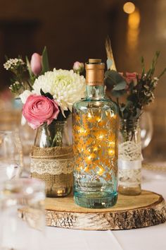 a bottle filled with lots of lights sitting on top of a wooden table next to flowers