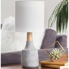 a table lamp sitting on top of a wooden table next to a white pillow and potted plant