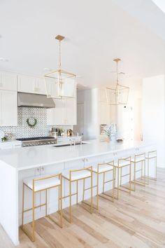 a large kitchen with white cabinets and gold accents on the countertops, along with wooden flooring