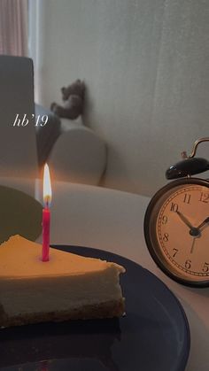 a slice of cake with a candle on it next to an alarm clock and a notepad