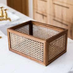 a wooden basket sitting on top of a white counter next to a faucet