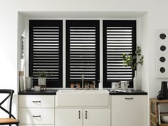 a kitchen with black and white shutters in it's window sill, next to a sink