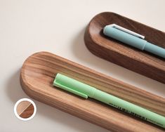 a wooden pen holder with two pens on it and a green marker in the middle