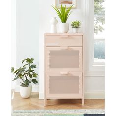 a pink cabinet with two plants on top and a potted plant in the corner