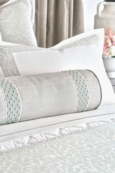 a bed with white and blue sheets, pillows and flowers on the headboard in front of a window