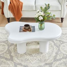 a white coffee table with flowers in a vase on top and a couch behind it