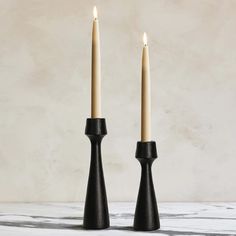 two black candlesticks sitting on top of a marble table next to each other