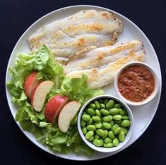 a white plate topped with an apple and salad next to some beans on a black table