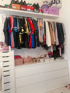 an organized closet with clothes and shoes hanging on the wall next to a chest of drawers