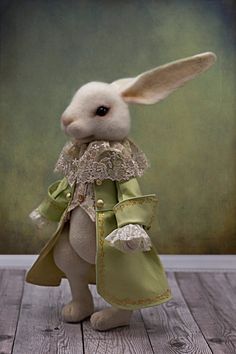 a stuffed rabbit dressed in green and white with lace on it's head, standing on a wooden floor