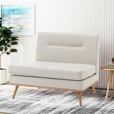 a white couch sitting on top of a rug next to a table and potted plant