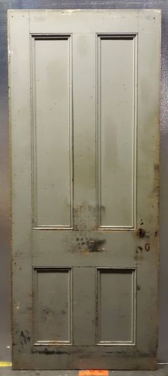 an old metal door with rusted paint on the bottom and side panels, in front of a gray wall