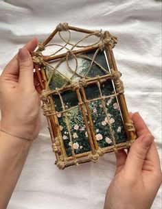 two hands holding an old stained glass and wood box with flowers on the outside, in front of a white sheet