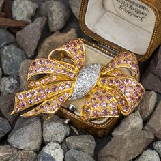 This lovely 18K yellow gold brooch features a bow motif and is accented with sixty-five (65) round single cut diamonds bead set into white gold. The ribbons are accented with one hundred eight (108), bead set, round mixed cut natural pink tourmalines. The brooch measures 60.0mm X 40.5mm. There is one diamond chipped but nothing that noticeably distracts from the beauty of the piece. Tourmaline Rings, Gold Brooch, Bead Set, 108 Bead, Gold Brooches, Tourmaline Ring, Unique Gemstones, Green Tourmaline, October Birth Stone