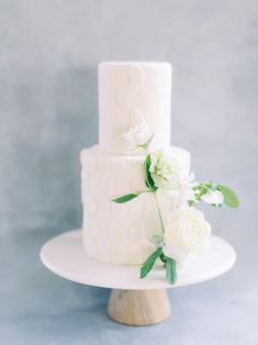 a three tiered white cake with flowers on the top and bottom, sitting on a wooden stand